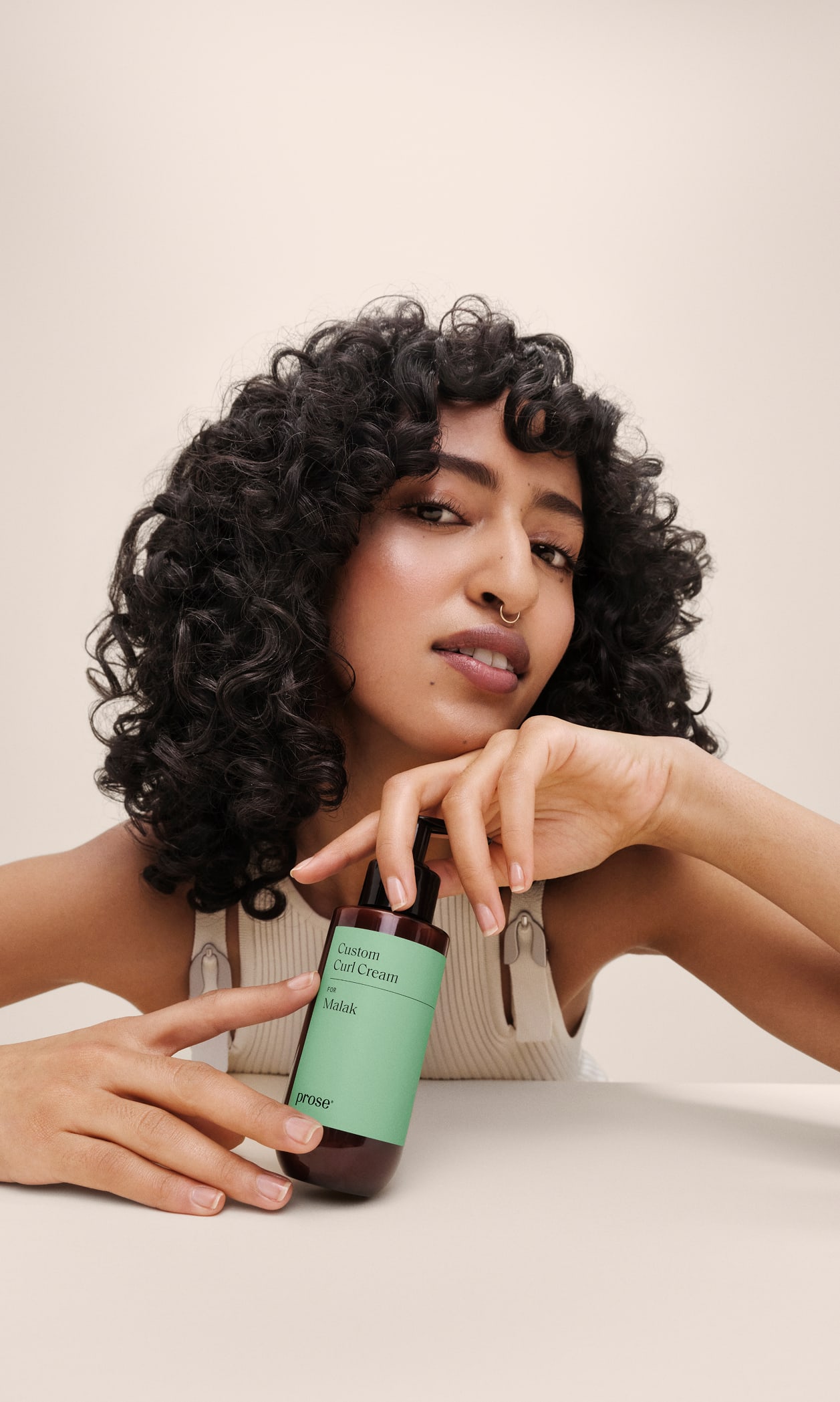 A woman with voluminous curls resting her hand on a Prose Custom Curl Cream bottle.
