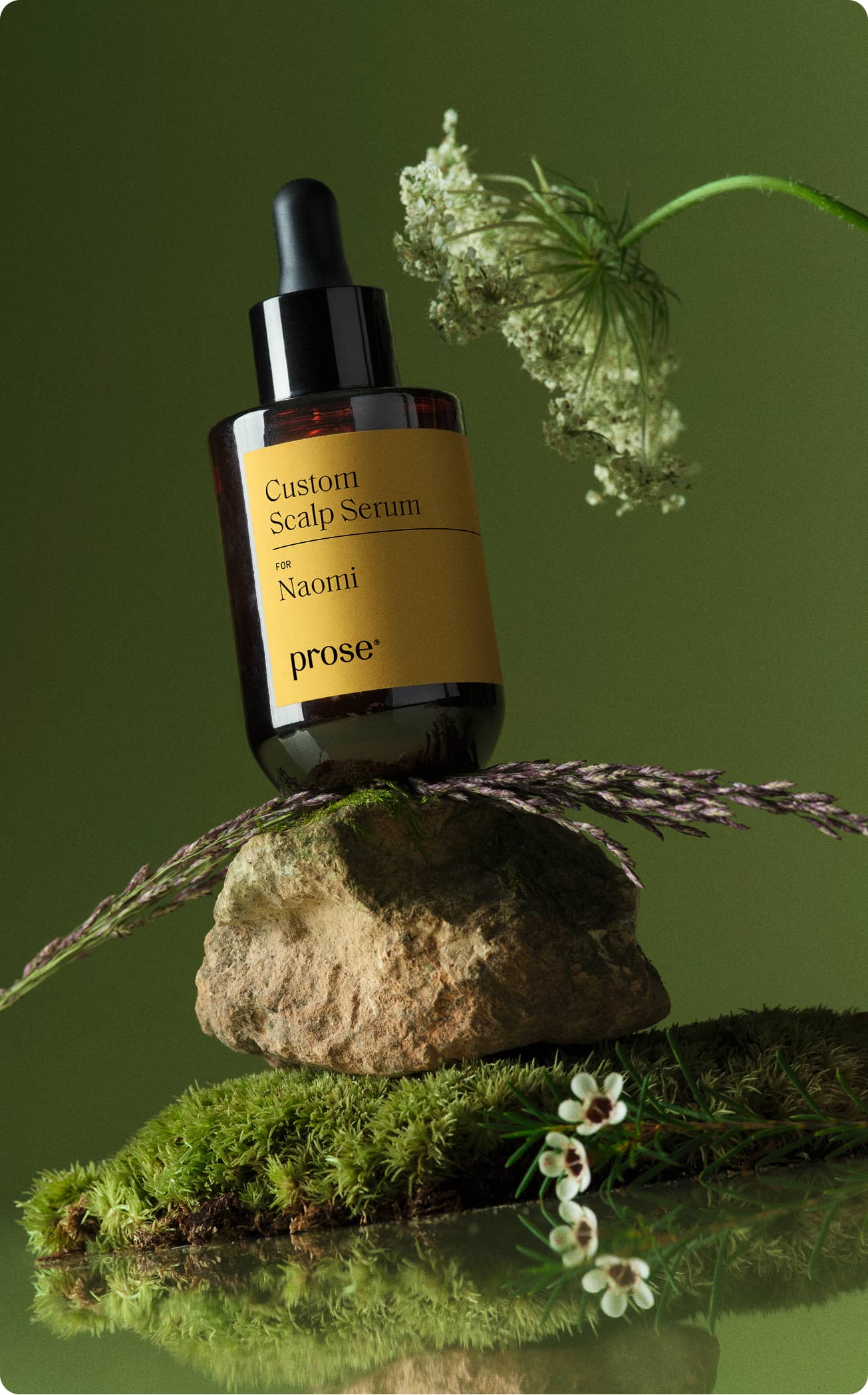 Close-up of a Prose Custom Scalp Serum bottle with ingredients and greenery.