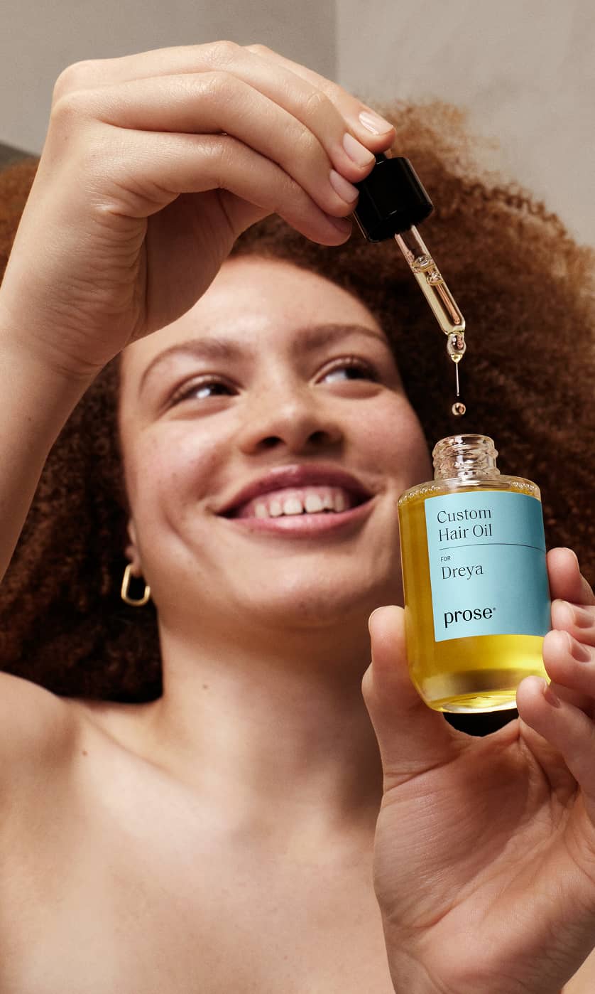 Smiling woman using Prose Custom Hair Oil with overlay text saying ’80_ saw less frizz using personalized Prose hair oil’